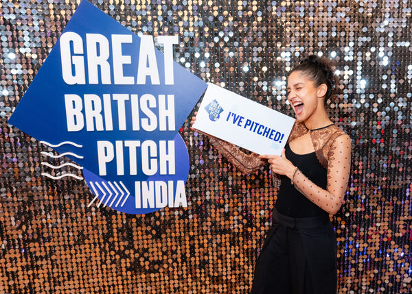 A small business owner holding an I've Pitched sign beside the Great British Pitch India logo
