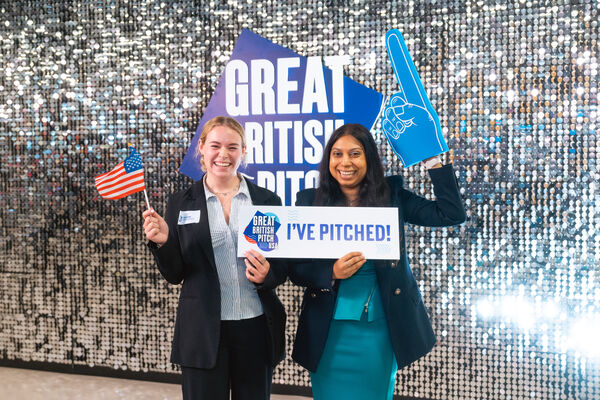 Two small business owners celebrating with an I've Pitched sign and a US flag in front of the sequin wall